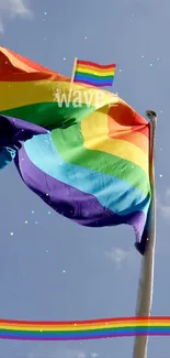 Vibrant rainbow Pride flag against a blue sky with colorful sparkles.