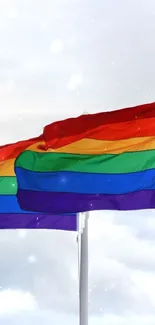 Vibrant rainbow pride flag waving against a bright blue sky.