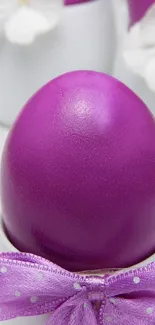 Purple Easter egg with ribbon and white flowers in background.