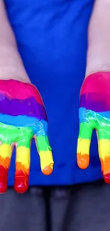 Hands covered in rainbow paint set against a bright red background.