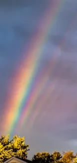 A vivid rainbow arches through a dramatic and stormy gray sky above sunlit rooftops.