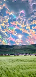 Vibrant rainbow clouds over a grassy field and distant mountains.