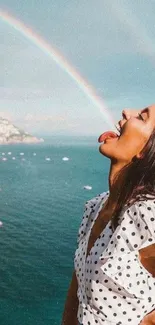 Woman enjoying a rainbow over a blue coastal landscape.