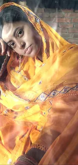 Rajasthani woman in orange traditional attire against a brick wall.