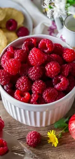 A bowl of vibrant red raspberries surrounded by flowers on wooden background.