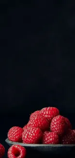 A dark background with vibrant red raspberries in a bowl.