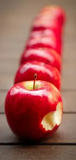 Line of red apples with a bite on a wooden surface.