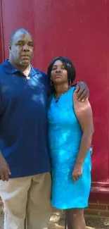 Couple posing in front of a red brick wall with blue and casual attire.