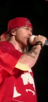 Performer in red shirt and cap singing passionately on stage.