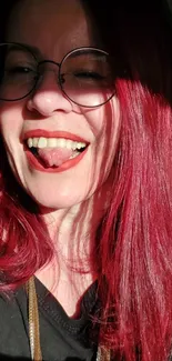 Smiling woman with red hair and glasses in bright light.