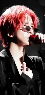 Red-haired performer in black attire with sunglasses, holding a red microphone.