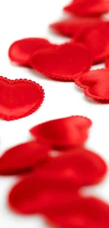 Mobile wallpaper with vibrant red fabric hearts on a white background.