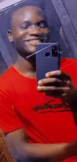 Smiling person in a red shirt taking a mirror selfie with a mobile.