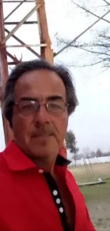 Man in a red shirt outdoors with natural backdrop.