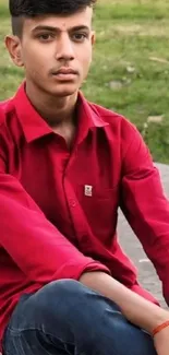 Young man in red shirt sitting outdoors against grassy background.