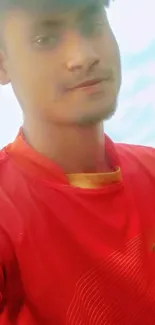 Person wearing a red shirt with a soft sky background.