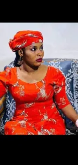 Woman in vibrant red traditional dress seated on patterned sofa.