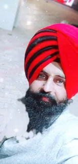 Man wearing a red turban in an outdoor setting, vibrant Sikh portrait.