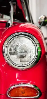 Close-up of a vibrant red vintage car with detailed chrome and headlight.