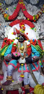 Colorful religious idol with garlands on a vibrant mobile wallpaper.