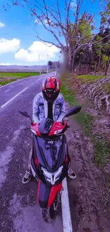 Person with red scooter on a countryside road under a vibrant blue sky.