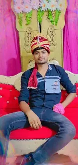 Man in festive attire on red sofa with vibrant backdrop.