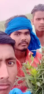 Three men in rural setting with green plants and colorful attire.