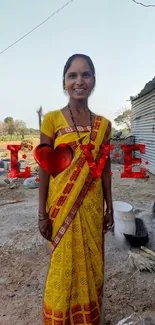 Woman in yellow sari with love theme on rural backdrop.