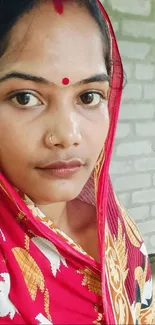 Woman in a red saree against a brick wall on mobile wallpaper.