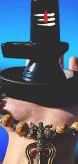 Hand holding a Shivling with beads on a vivid blue background.