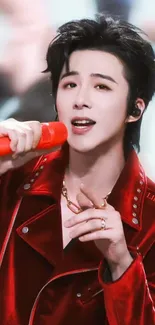 Singer in a red jacket performs passionately with a red microphone.