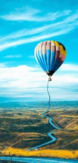 Hot air balloon soaring above a winding road with a vivid blue sky.