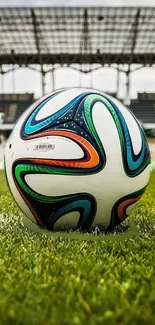 Soccer ball on green field with stadium in background.