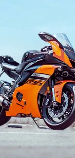 Orange and black sports bike on pavement with sky background.