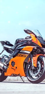 Vibrant orange Yamaha R6 sports bike under clear blue sky.