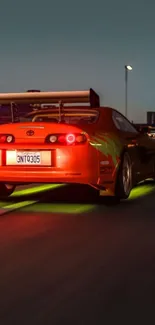 Orange sports car with neon lights on urban road at night.