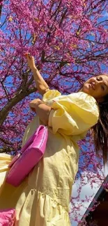 Woman in yellow dress under vibrant pink tree.