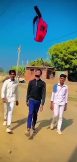 Three people toss a backpack on a sunny street under a bright blue sky.