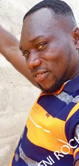 Man in vibrant orange and blue striped shirt against a textured wall.