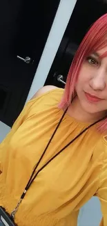 A person with pink hair in yellow outfit selfie.