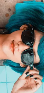 Woman with blue hair and sunglasses by the pool.