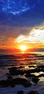 Vibrant sunset over a calm ocean with a colorful sky and rocks in the foreground.