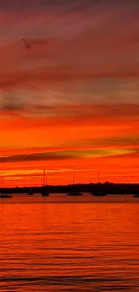 Beautiful sunset over harbor with boats and vivid orange sky.