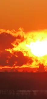 Sun setting over horizon with vibrant orange clouds.