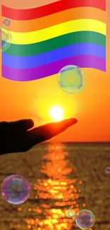 Hand holds the sun under a rainbow flag at sunset with bubbles floating.