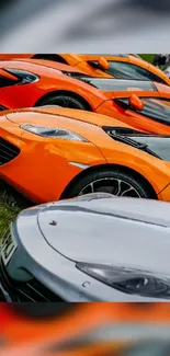 Lineup of vibrant sports cars in orange and silver on grass.