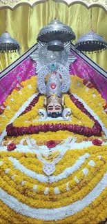 Vibrant mobile wallpaper of a deity adorned with gold and floral decorations in a temple.