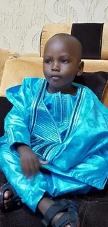 Child in vibrant blue traditional attire sitting on a couch.