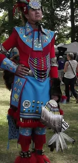 Man in vibrant red and blue traditional attire with feathers and accessories.