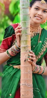 Woman in vibrant traditional attire leaning against a tree, green background.